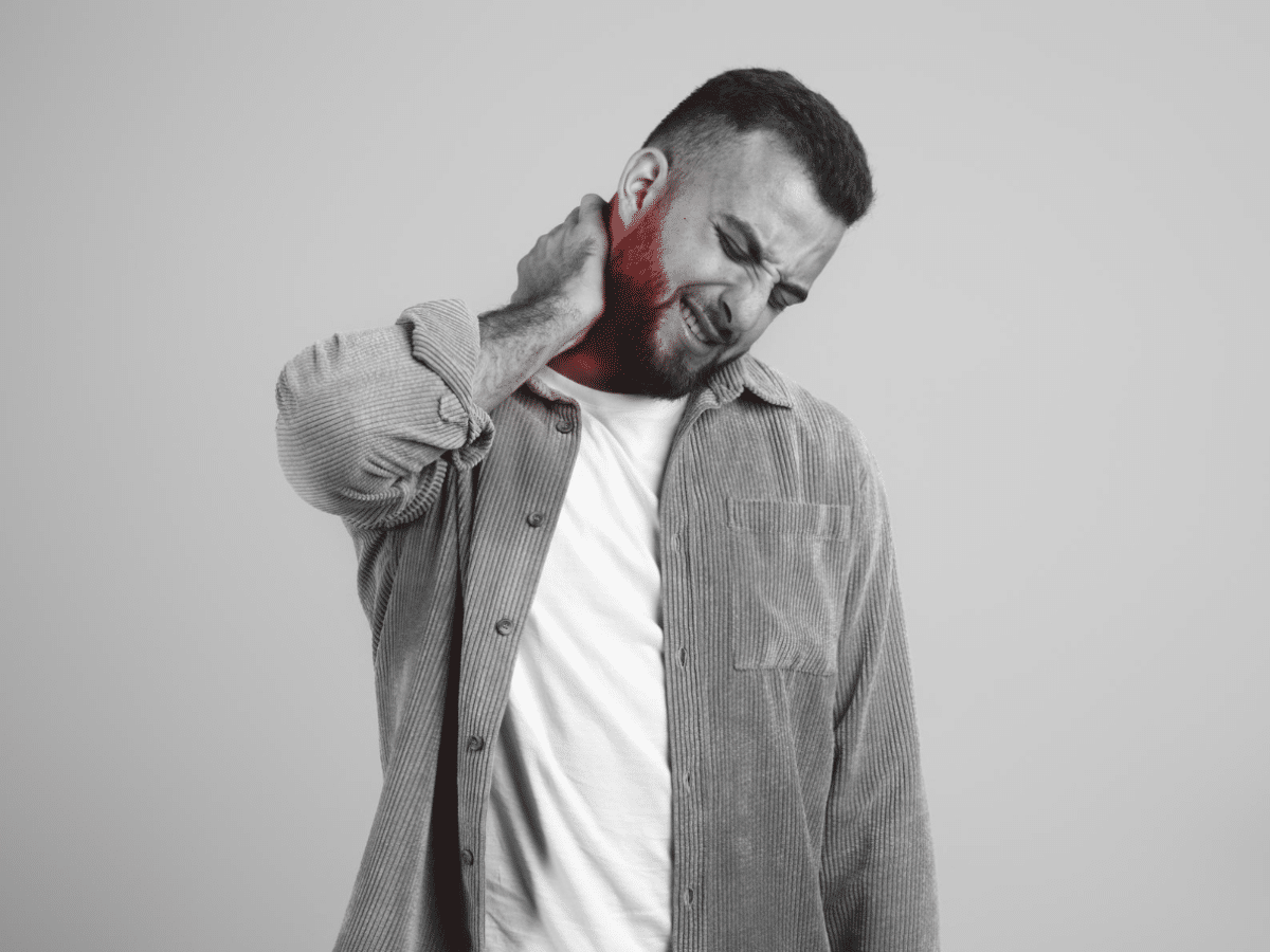 A man with a pained expression is massaging his sore neck, pressing into the muscles for relief.